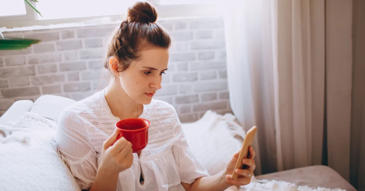 Person checking a menstrual cycle tracking app while holding a cup of tea