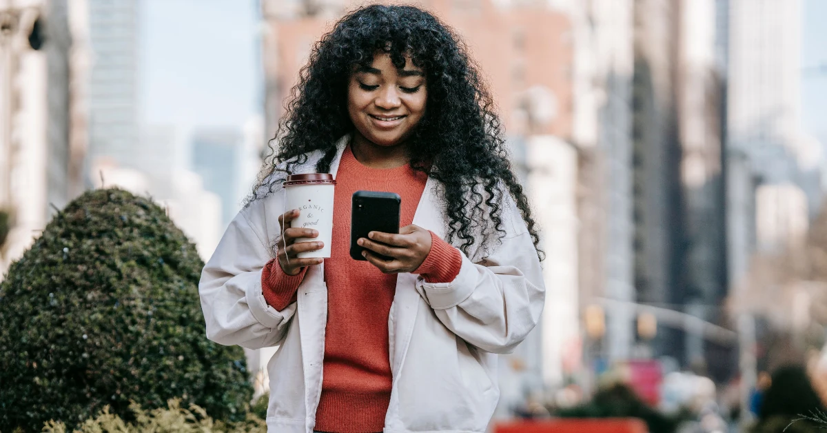 Woman tracking cycle symptoms and energy levels on a phone app while making tea