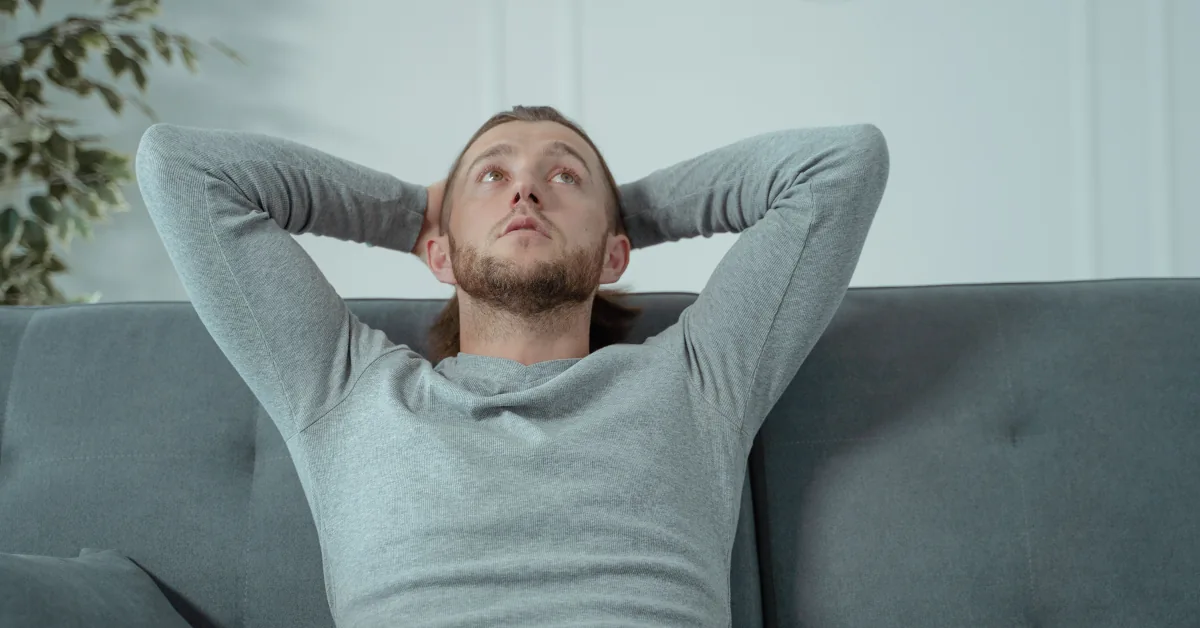 A person resting on a couch in the afternoon with a glass of water nearby in a calm home setting, showing a moment of relaxation and tiredness.