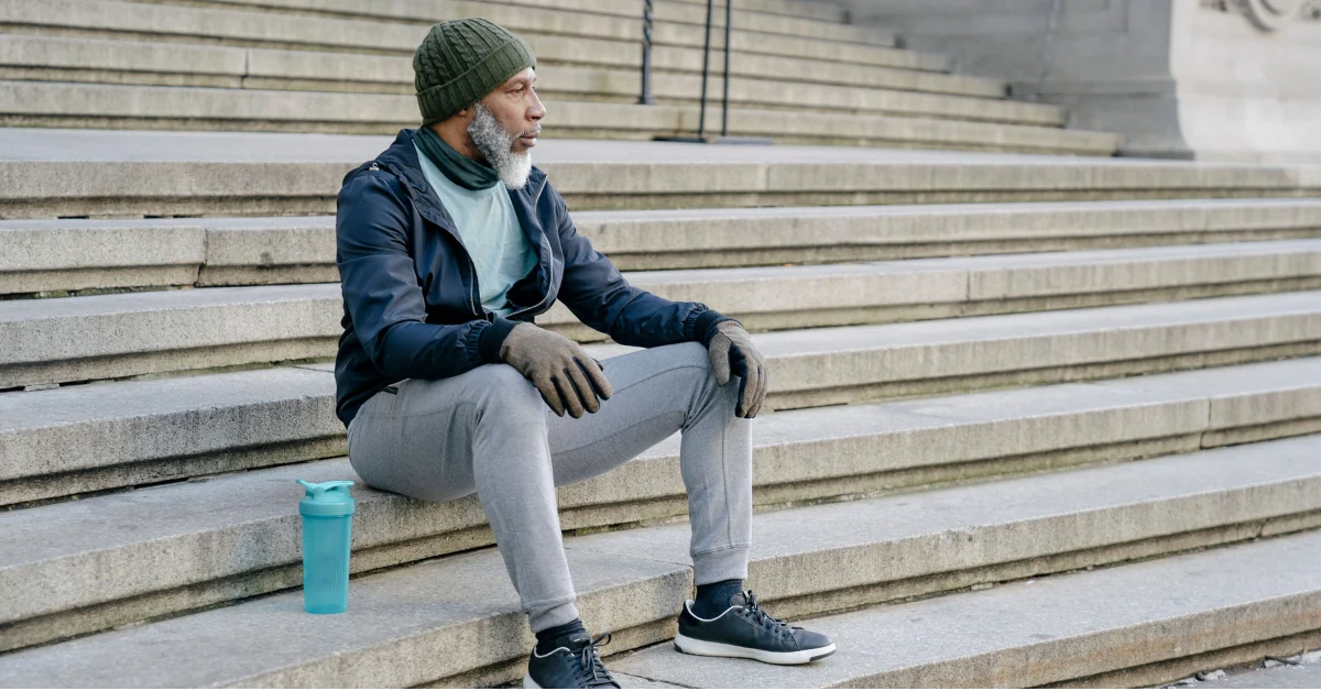 A person pausing halfway up a staircase and catching their breath during a normal daily activity, showing mild fatigue in a natural home or public setting.