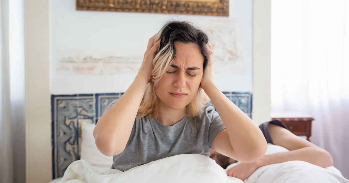 A person sitting on the edge of a bed in the morning with their head in their hands, showing everyday tiredness and low energy in a natural home setting.