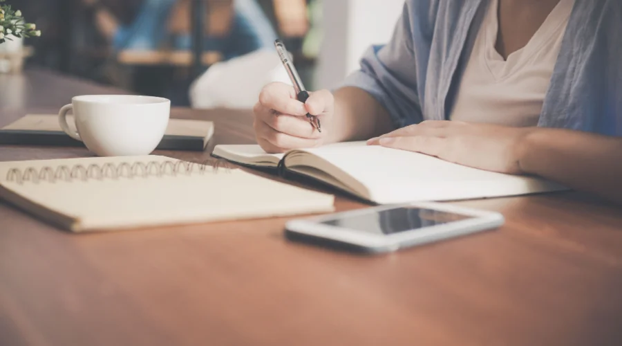 Person journaling at a table with a glass of water nearby