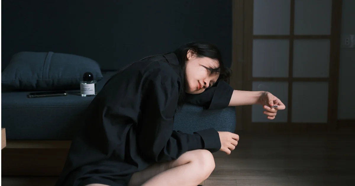 A person lying down in a dim quiet room with an arm covering their eyes, resting after experiencing a migraine attack.