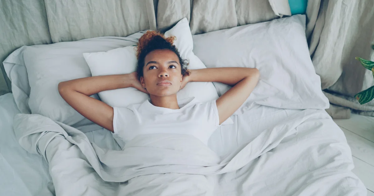 A young woman resting with a heating pad on her lower abdomen, calm bedroom light, dignified and not distressing