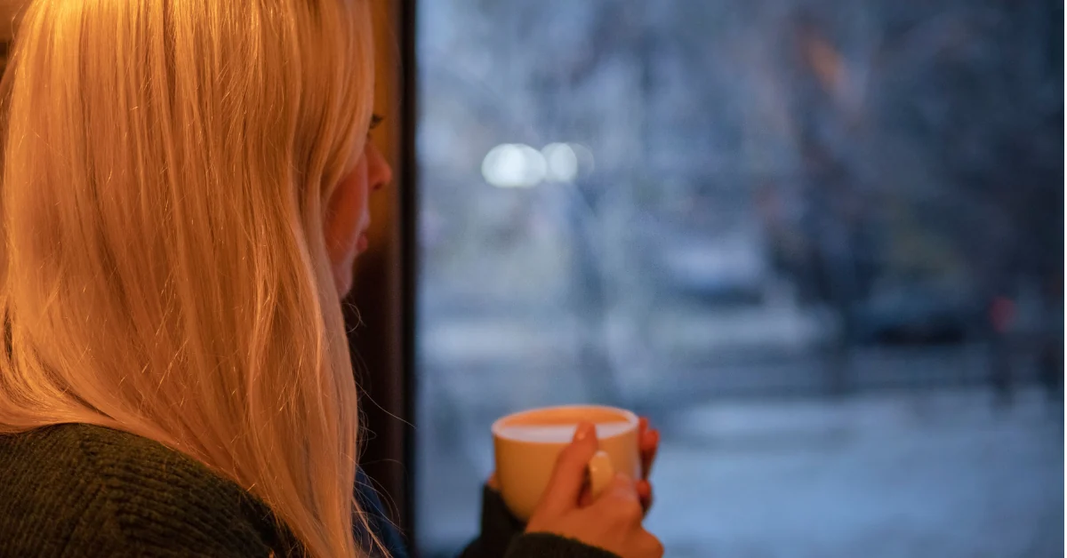 Person at a window on a grey winter morning holding a mug