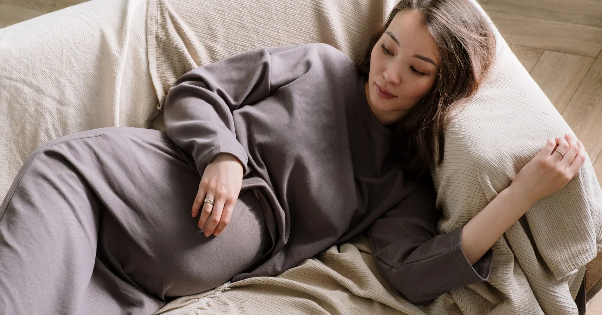 Pregnant woman resting on a sofa in soft daylight with her hand on her belly