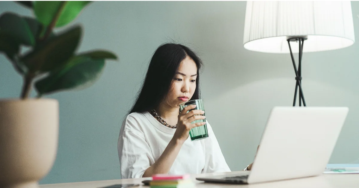Person sitting at a desk in the afternoon with an empty water bottle beside a laptop