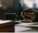 Hand holding a coffee cup at a desk in the mid-afternoon