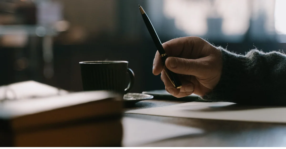 Hand holding a coffee cup at a desk in the mid-afternoon