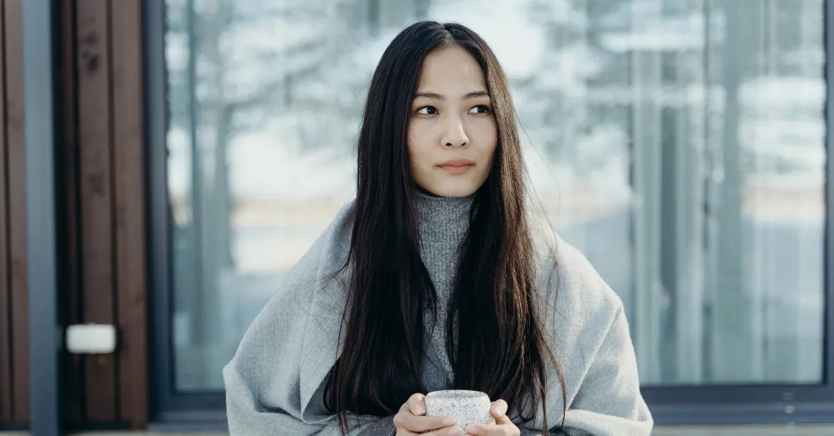 Person standing by a window on a grey winter morning holding a mug